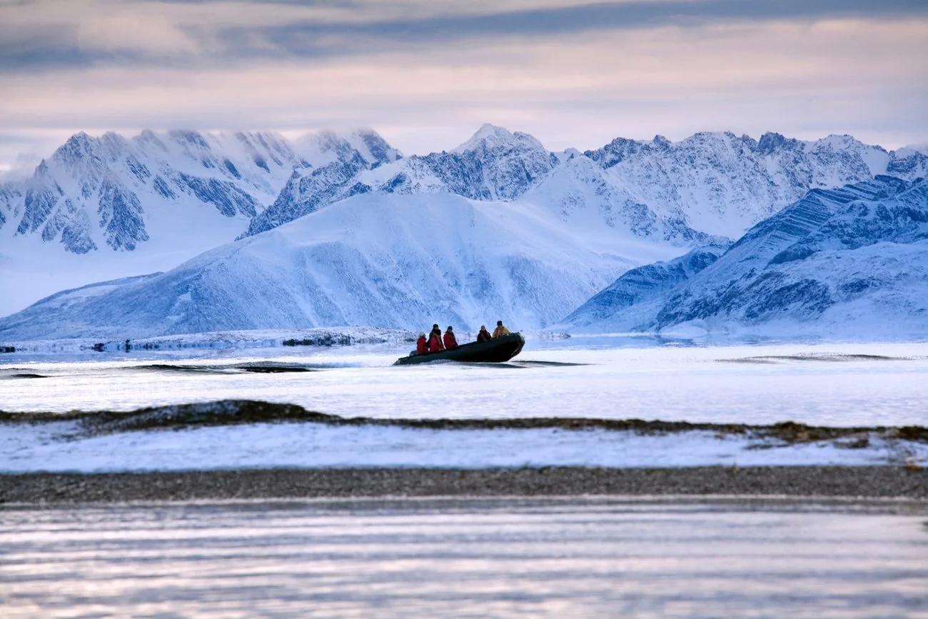 Expedition boat crossing Arctic waters beneath snow-covered mountains